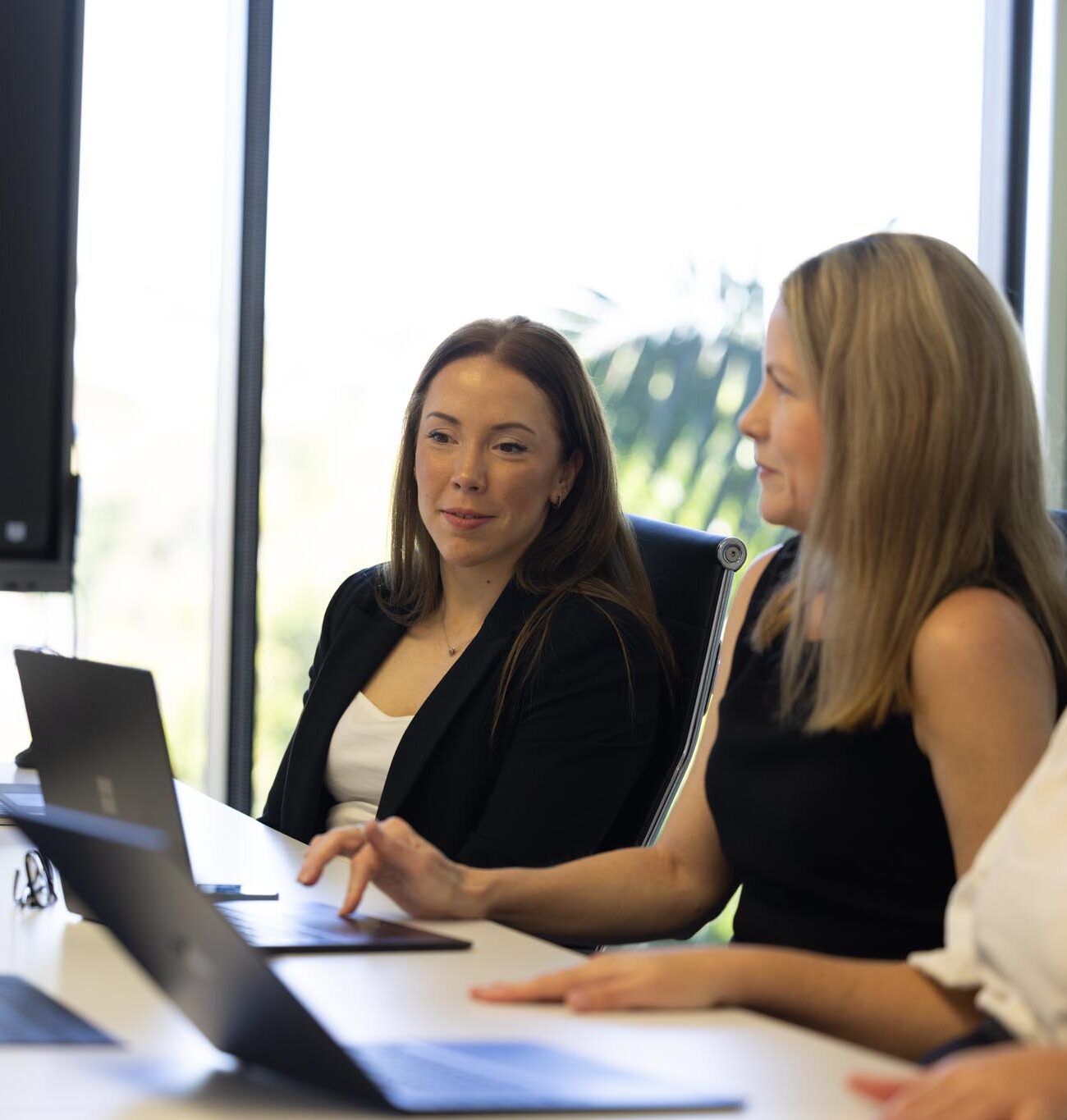 2 office ladies seated at a desk looking at a laptop